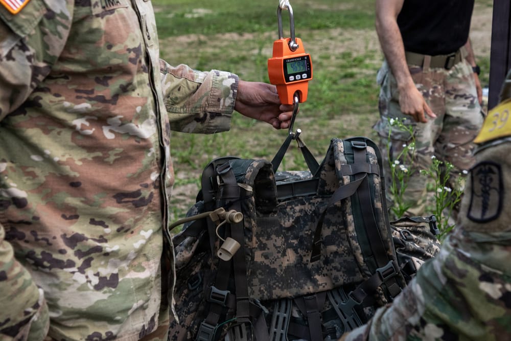 A rucksack hanging from an orange digital scale as its weight is verified after a ruck march.